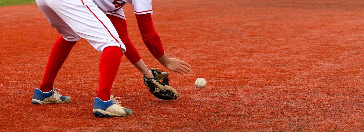 A high school baseball player fielding the ball on red turf field during a game
